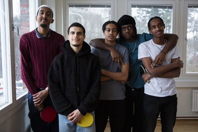 Portrait of multi-ethnic friends with table tennis rackets standing in games room