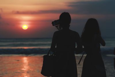 Silhouette woman standing on beach against sky during sunset