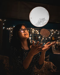 Young woman gesturing while sitting against moon at night