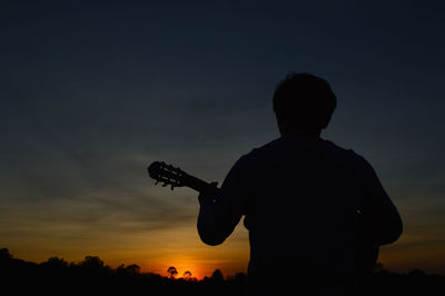 A man with a guitar strumming and looking at the sunset in the evening