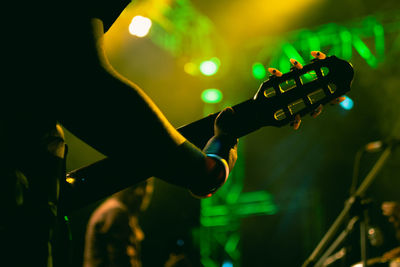 Close up of a hand holding a guitar neck at a concert with green lights in the background
