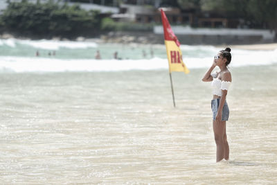 Young woman standing at beach against sky