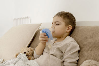 Sick little boy with inhaler for cough treatment. unwell kid doing inhalation on his bed. flu season