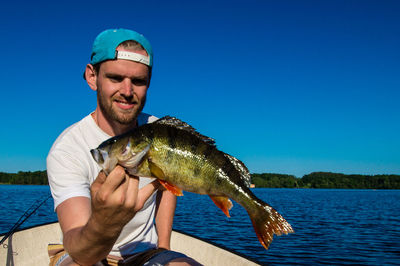 Man holding fish on boat at lake against clear blue sky