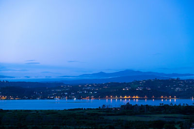 Illuminated city by sea against sky at night