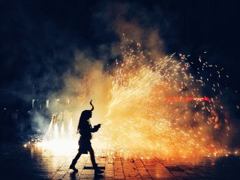 Silhouette person walking against illuminated firework at night