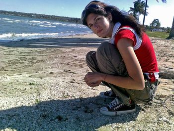 Young woman sitting on sand at beach against sky