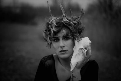 Portrait of woman with horns holding animal skull in forest