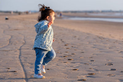 Side view of baby girl with mouth open standing at beach during sunset