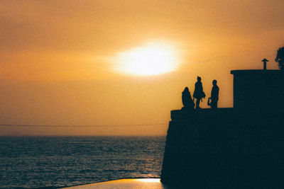 Rear view of silhouette people against sea at sunset