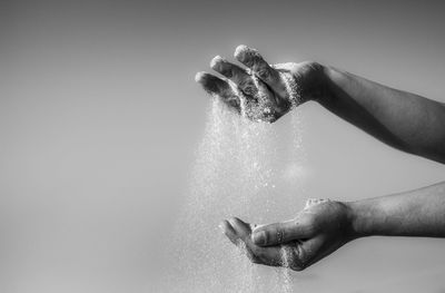 Cropped image of hands dropping sand against cloudy sky