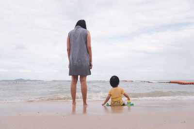 Rear view of friends on beach against sky