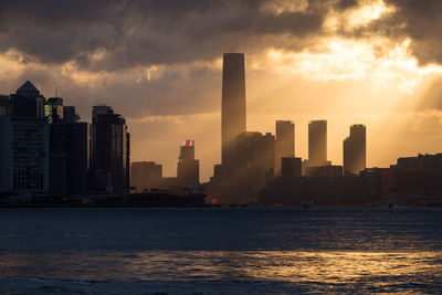 Sea by modern buildings against sky during sunset