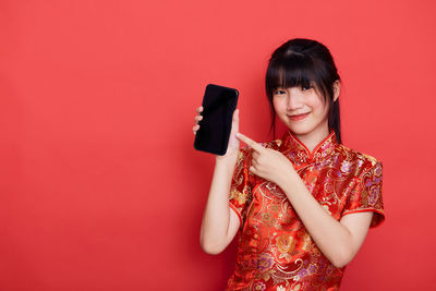 Portrait of smiling woman holding smart phone against red background