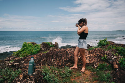 Woman standing on rock at beach against sky