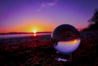 Close-up of crystal ball on beach during sunset