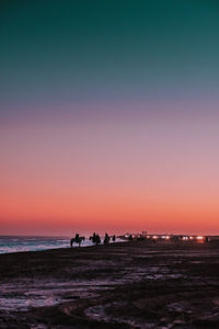 Horses and tourists at beach against sky during sunset