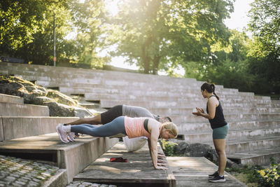 Side view of female instructor motivating team while doing push-ups on steps