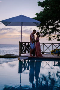 Couple standing by swimming pool against sky