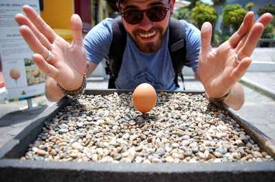 Young man with brown egg on pebbles in container