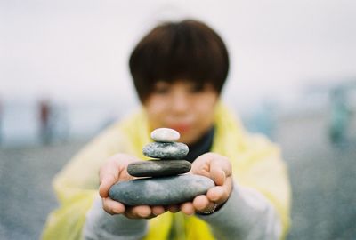 Woman holding stack on pebbles at beach against sky