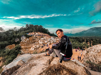 Young man sitting on rock against mountain