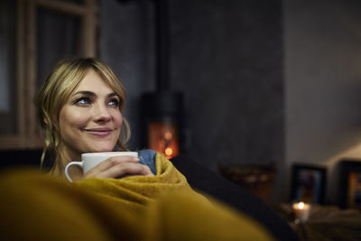 Portrait of smiling woman with cup of coffee relaxing on couch at home in the evening