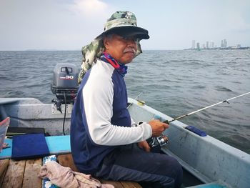 Man sitting on boat while fishing in sea against sky