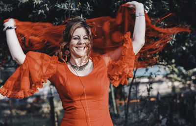 Smiling woman looking away while holding scarf against trees