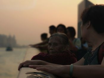 Rear view of people sitting on shore against sky during sunset