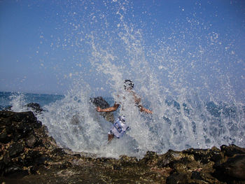 Waves splashing on man standing at beach against sky