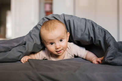 Surprised baby lies on the bed under the blanket