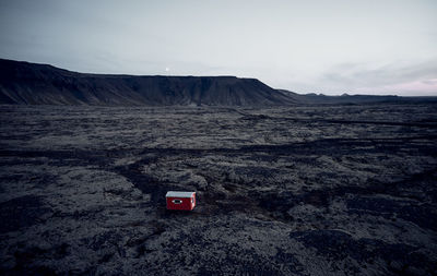 Small red house in dark dry terrain surrounded by hills