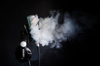 Close-up of smoke by microphone and headphones against black background