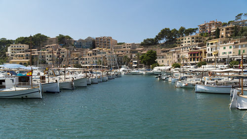 Sailboats moored in harbor by buildings against clear sky