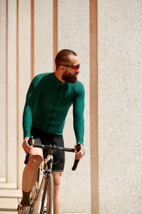 Portrait of young man riding bicycle against wall