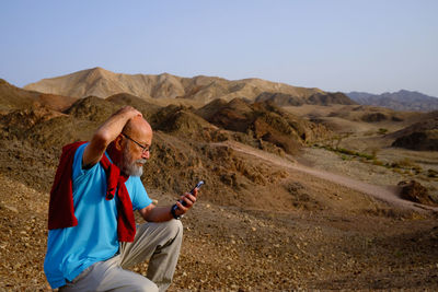 Side view of woman using mobile phone while standing on mountain against clear sky