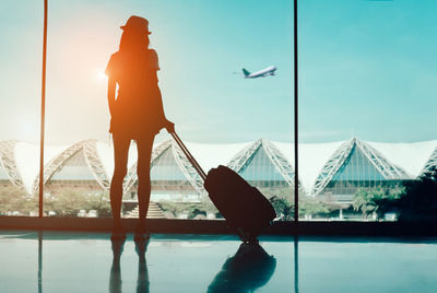 Rear view full length of woman standing holding luggage at airport departure area