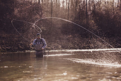 Mid adult man throwing fishing reel in river to catch fish during sunset