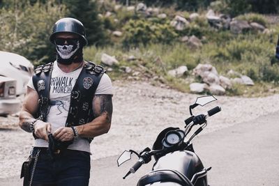 Man wearing mask and helmet standing by motorcycle on road