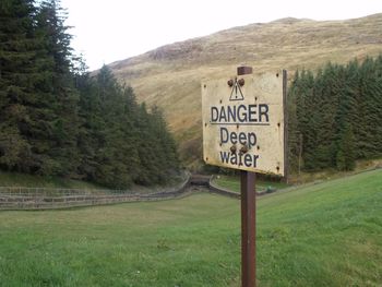 Close-up of warning sign on grassy field against mountains