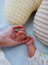 Cropped image of child holding mother hand on bed at home