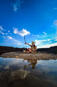 People sitting on rock by water against sky