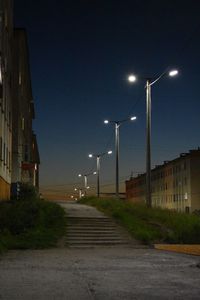 Illuminated street lights in city against clear sky at night