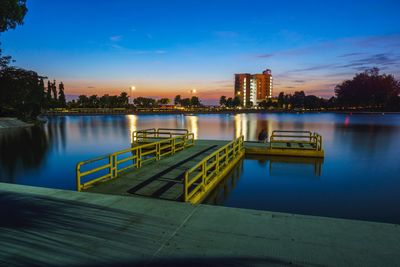 Illuminated city by river against sky at sunset