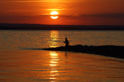 Silhouette man by sea against sky during sunset