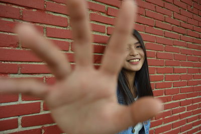 Portrait of smiling young woman showing stop gesture against red brick wall