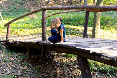 Full length of girl sitting on bench against trees