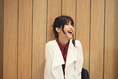Young woman laughing against wooden wall