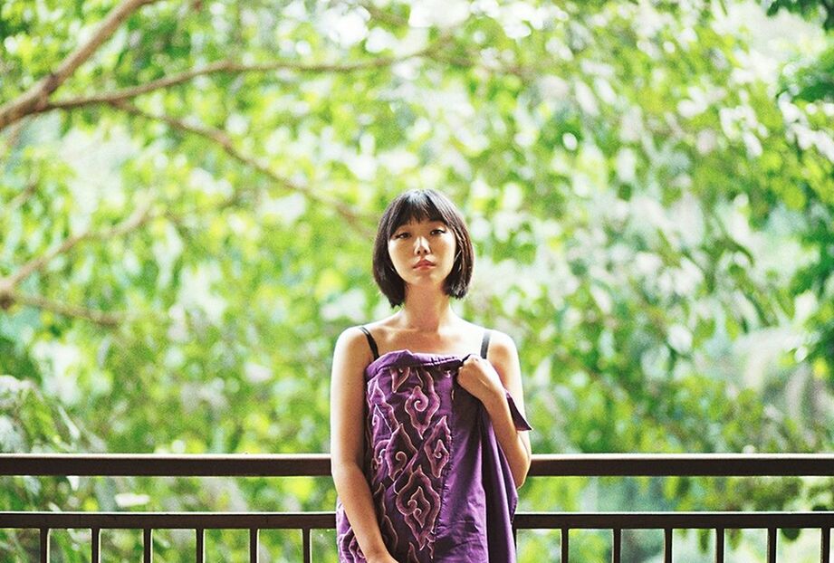 YOUNG WOMAN STANDING IN FRONT OF TREE